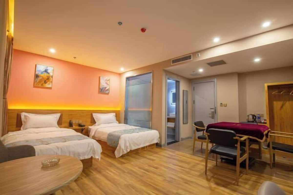 Quarto de hotel com duas camas, uma mesinha, uma cadeira e uma porta para o banheiro.