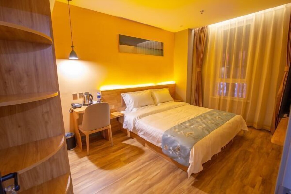 Una habitación de hotel con un escritorio de madera, una cama con colcha estampada, una obra de arte en la pared y una ventana con cortinas.