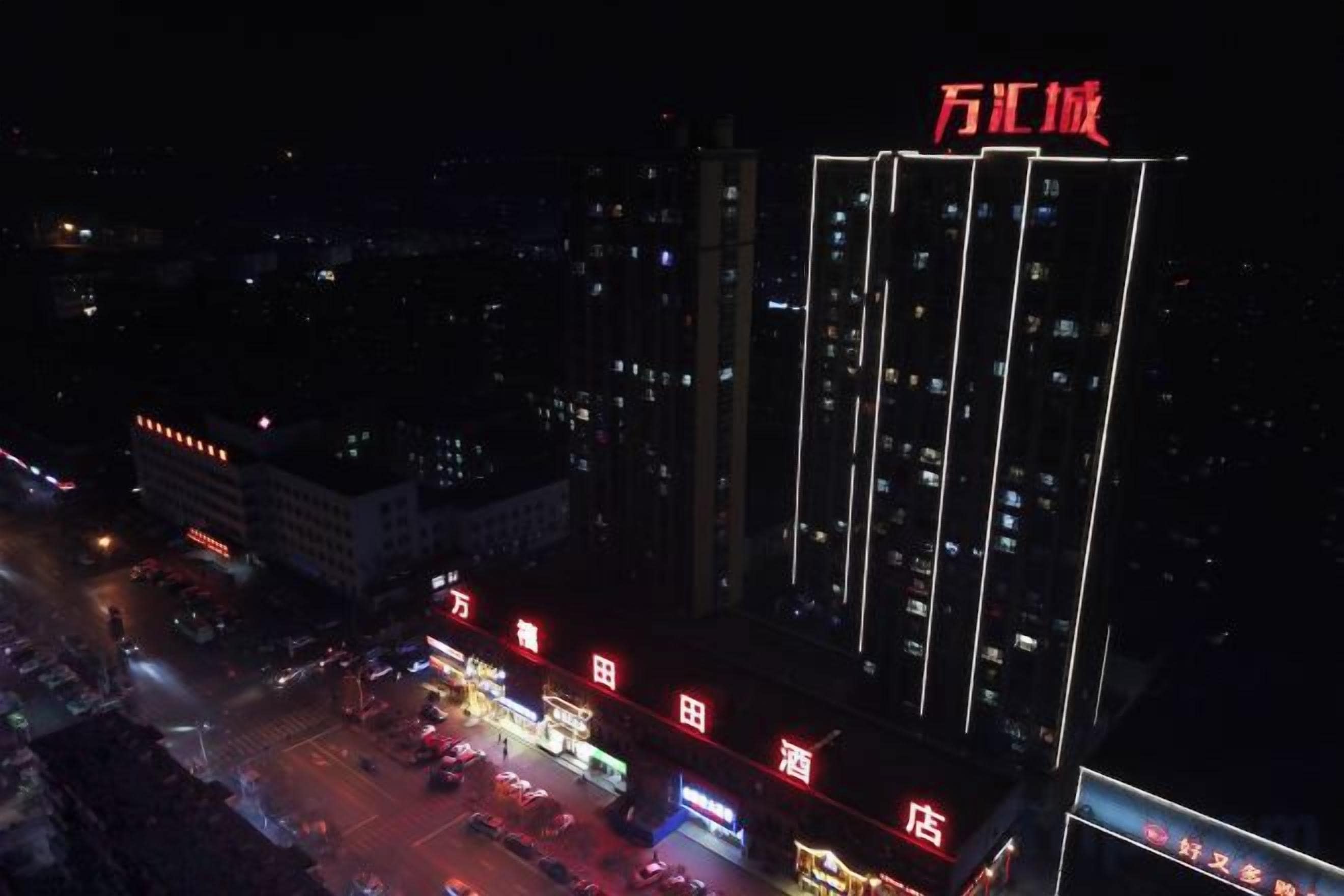 A high-rise building with illuminated signage and a parking lot.