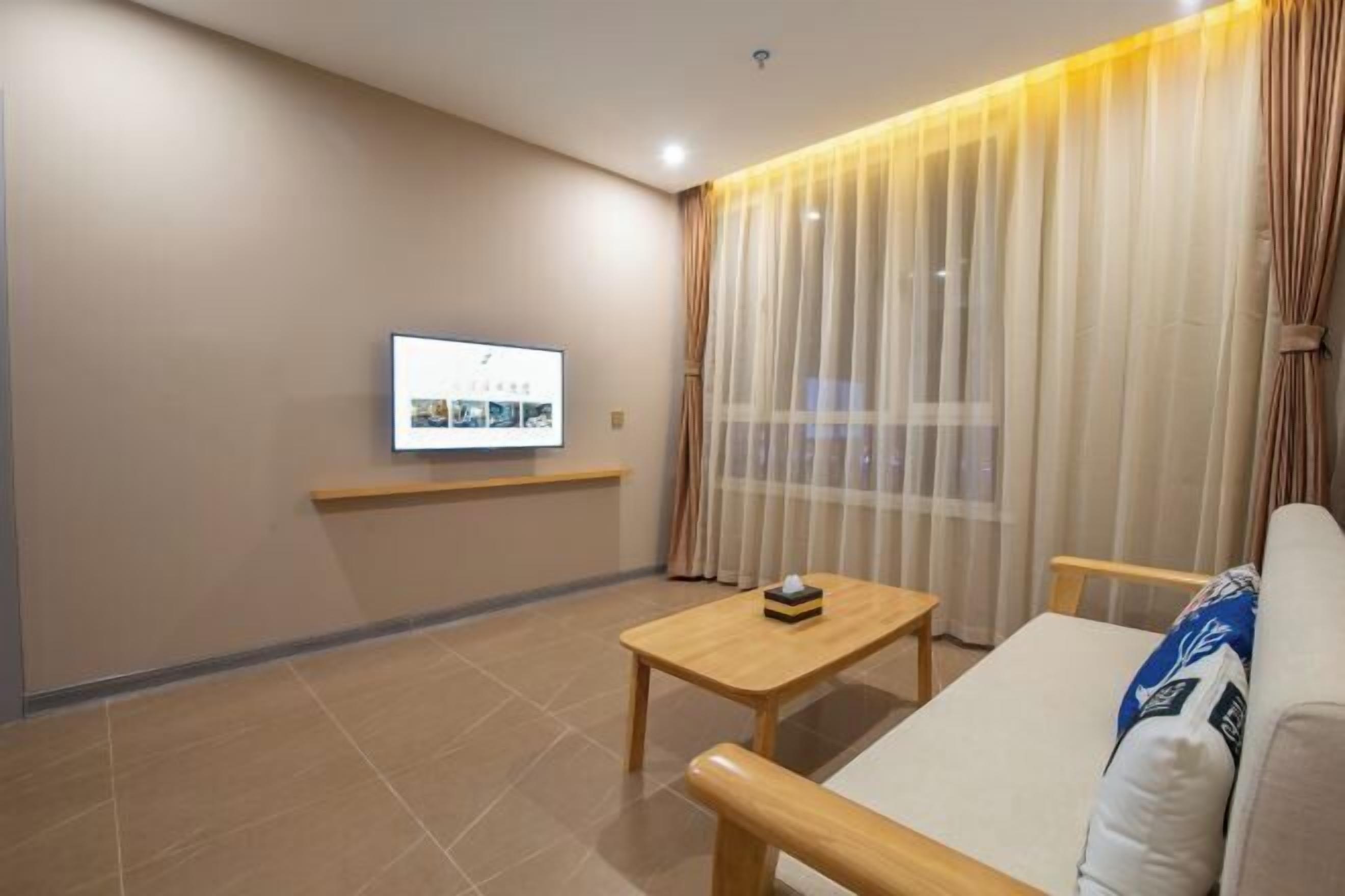 Una sala de estar moderna con un televisor de pantalla plana montado en la pared, una mesa de centro de madera, un sofá y cortinas de gasa.