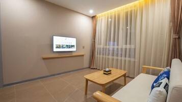 Una sala de estar moderna con un televisor de pantalla plana montado en la pared, una mesa de centro de madera, un sofá y cortinas de gasa.