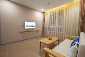 Una sala de estar moderna con un televisor de pantalla plana montado en la pared, una mesa de centro de madera, un sofá y cortinas de gasa.