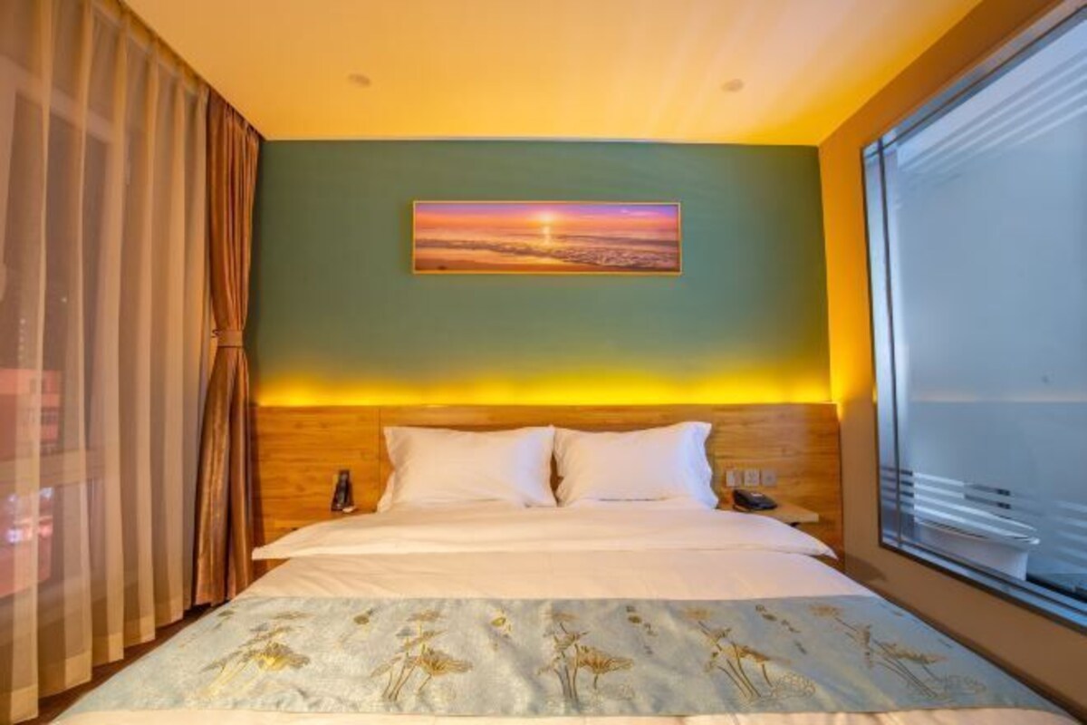 Una habitación de hotel con una cama, un cuadro en la pared y una ventana con cortinas.