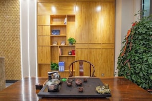A wooden table with teapots and a teapot set, a chair, and a bookshelf with various items. - Wanxi Tiantian Hotel (Shenyang)