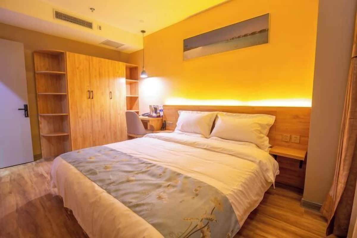 Quarto com cama, guarda-roupa de madeira, mesa de cabeceira, abajur e um quadro na parede.