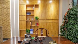 A wooden table with teapots and a teapot set, a chair, and a bookshelf with books and decorative items. - Wanxi Tiantian Hotel (Shenyang)