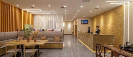 A hotel lobby with a reception desk, seating area, and a television screen.