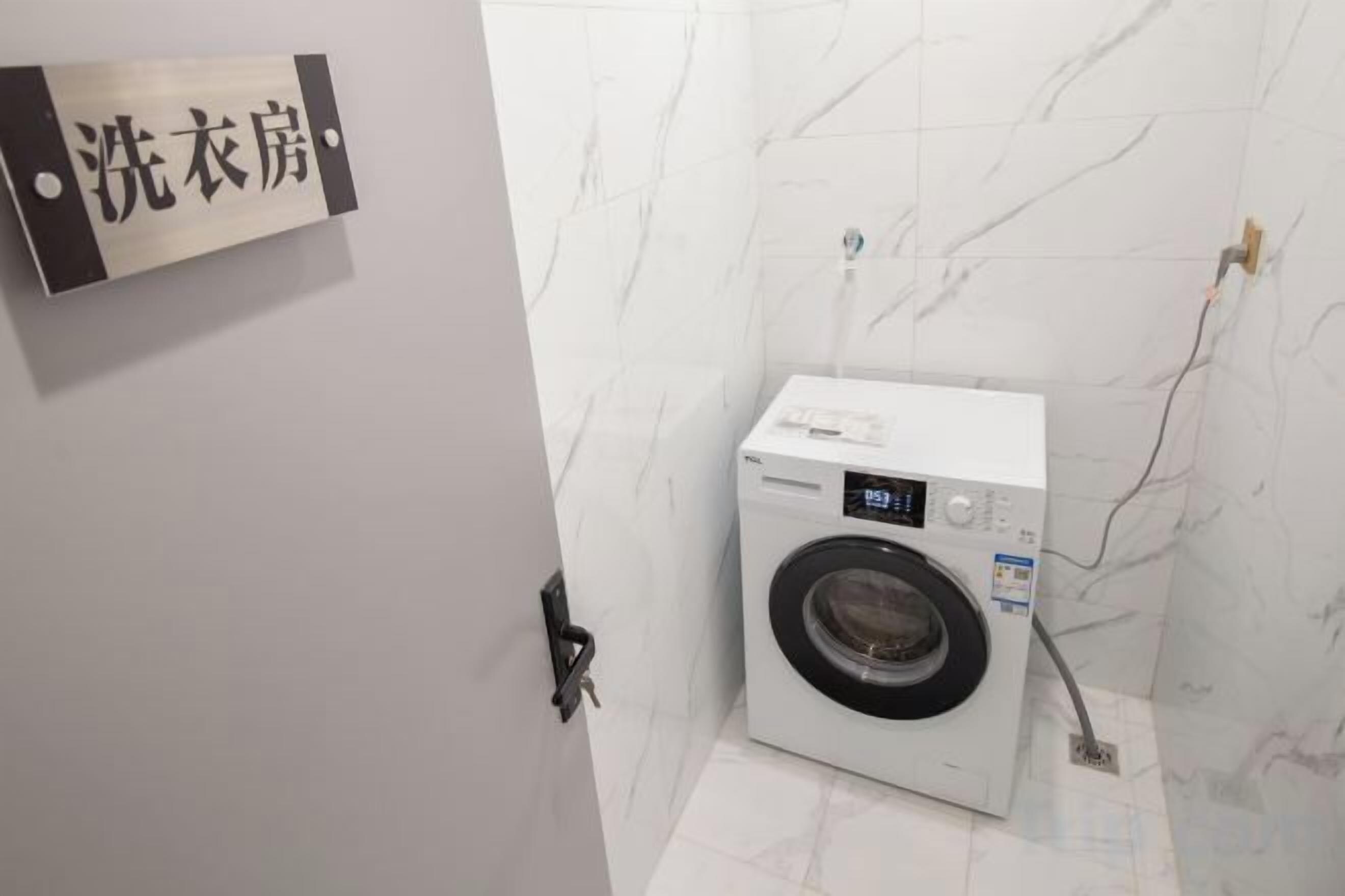 A compact, modern laundry room with a washing machine, a wall-mounted sign, and a marble-tiled floor.