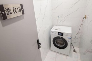 A compact, modern laundry room with a washing machine, a wall-mounted sign, and a marble-tiled floor. - Wanxi Tiantian Hotel (Shenyang)