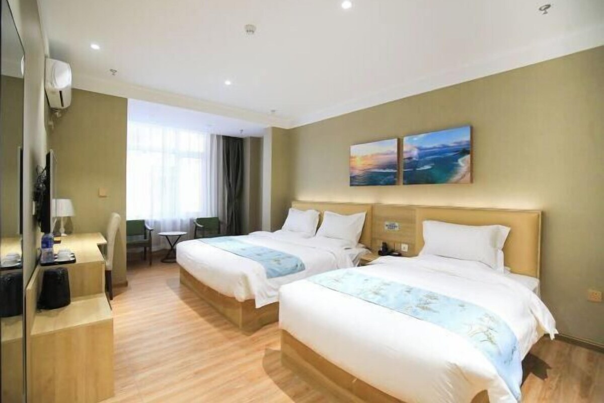 Habitación de hotel con dos camas, un escritorio con silla, una mesita y una ventana con cortinas.