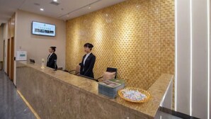 A reception desk with a digital screen displaying information, a patterned wall, and a reception area with a counter and a basket of items. - Wanxi Tiantian Hotel (Shenyang)