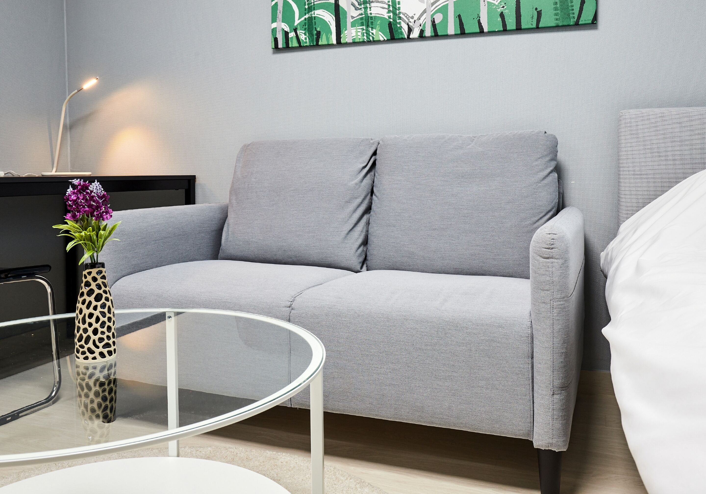 Un salón moderno con un sofá gris, una mesa de centro de cristal y un jarrón decorativo con flores moradas.