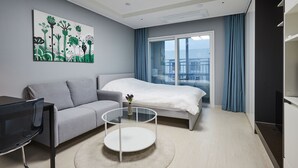 A modern hotel room with a bed, a sofa, a TV, and a painting on the wall.