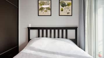 Ein Bett mit weißer Matratze und schwarzem Kopfteil in einem Zimmer mit grauer Wand. An der Wand befinden sich zwei gerahmte Pflanzenbilder.
