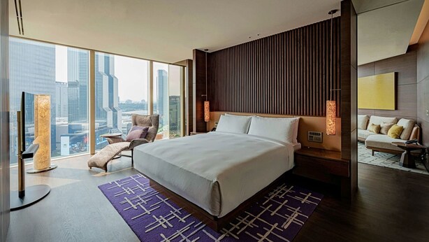 A modern hotel room with a large bed, city view, and a cozy seating area.