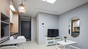 A modern living room with a flat-screen TV, white furniture, a mirror, and a ceiling light fixture.