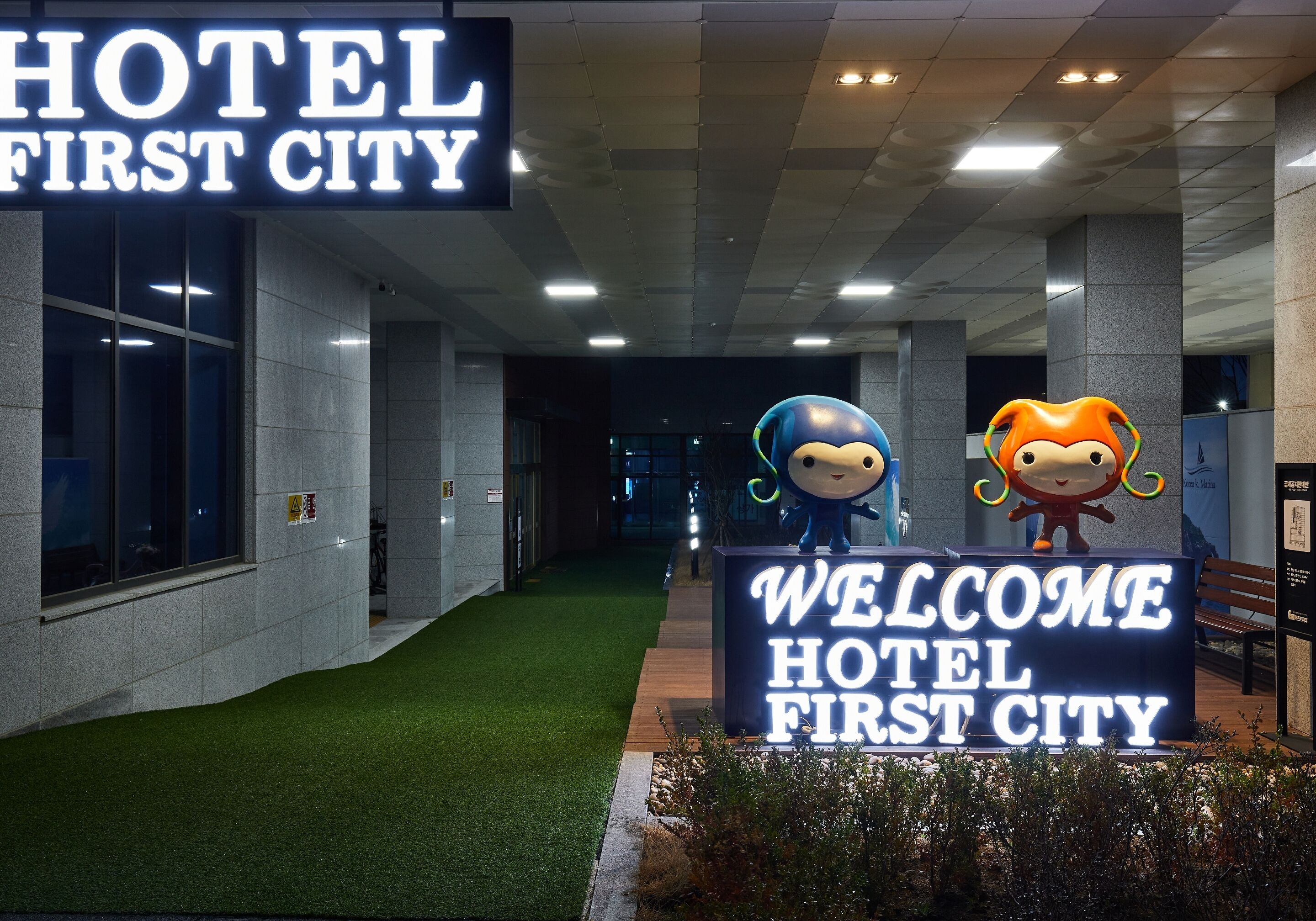 En hotellentrél med en skylt som visar texten ”VÄLKOMMEN TILL FIRST CITY HOTEL” och två tecknade figurer.