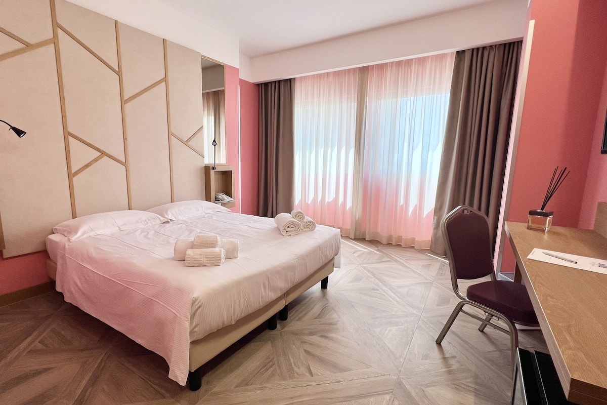 Een hotelkamer met een bed, een bureau, een stoel en een groot raam met gordijnen.