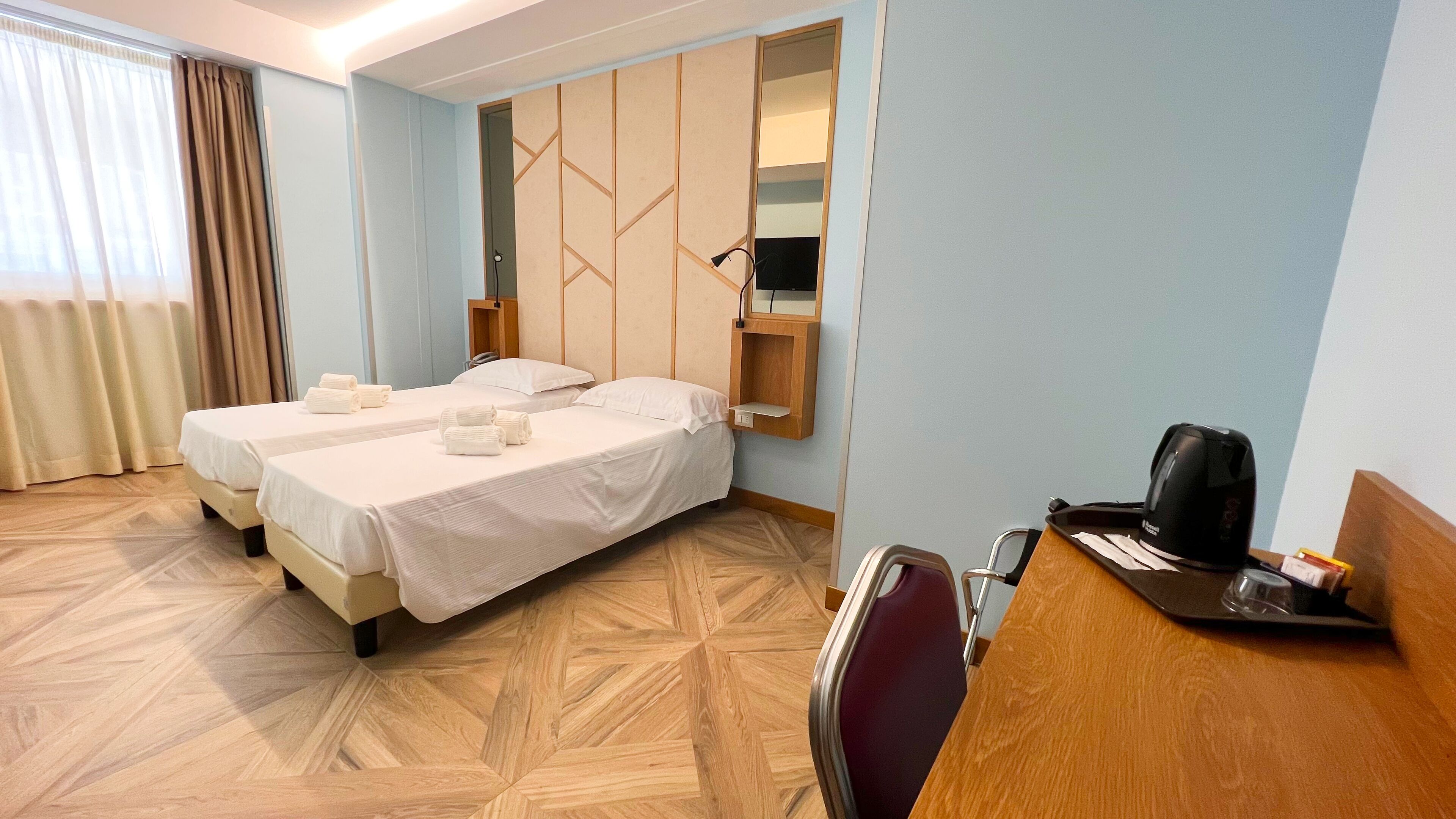 Habitación de hotel con dos camas, un escritorio con silla, un espejo y una cafetera.