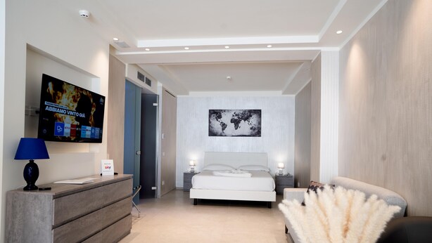 A modern hotel room with a large bed, a desk with a flat-screen TV, a bedside table with a lamp, and a decorative plant. - Catania Sea Palace Hotel (Catania)