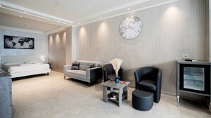 A modern living room with a bed, sofa, armchair, coffee table, and a TV stand. - Catania Sea Palace Hotel (Catania)