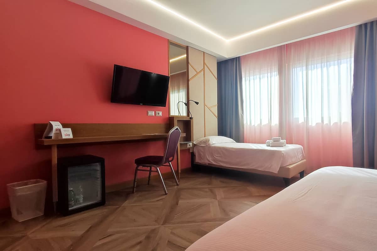 Een hotelkamer met een bed, een bureau met stoel, een televisie en een kleine koelkast.