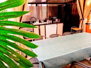 A dining area with a table set for two, a kitchen in the background, and a view of the outdoors.