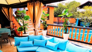 A curved sofa with blue cushions, a wicker chair, and a table with a green tablecloth. - All Inclusive Luxury Villa With sea View (Sozopol)