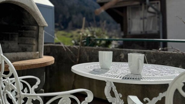 A round table with two white cups, a stone oven, and a mountainous backdrop. - Studio by Apartments Capricorn (Gsteigwiller)