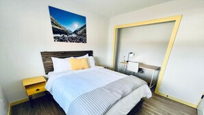A neatly arranged hotel room with a large bed, a bedside table, a desk with a chair, and a wall-mounted lamp. - Glacier Lake 2nd floor 2 bdrm condo (Joseph)