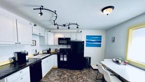 A compact kitchen with white cabinets, a black refrigerator, a microwave, and a dining area with a white table and chairs. - Glacier Lake 2nd floor 2 bdrm condo (Joseph)