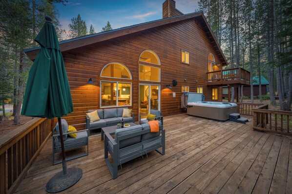 A wooden cabin with a deck, outdoor seating, and a hot tub.