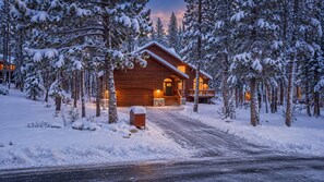 A wooden cabin with a porch, surrounded by snow-covered trees.