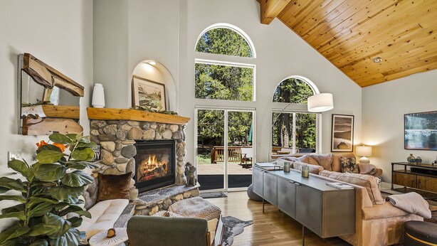 A spacious living room with a stone fireplace, large windows, and a high ceiling. - Chic Pet-Friendly Retreat | King Suite, Hot Tub | Clubhouse Access | Near Lake (Truckee)