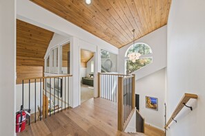 A spacious interior with wooden flooring, a staircase with a wooden railing, and a view of the outdoors through a large window. - Chic Pet-Friendly Retreat | King Suite, Hot Tub | Clubhouse Access | Near Lake (Truckee)