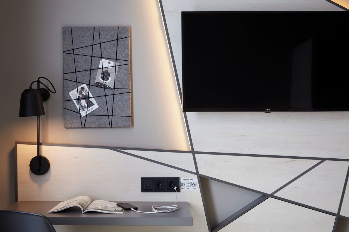 A modern room with a bed, a bedside table with a book, a lamp, and a wall-mounted TV.