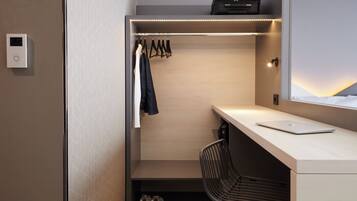 A compact, modern room with a built-in desk, a chair, a hanging closet with clothes, and a window with a view.