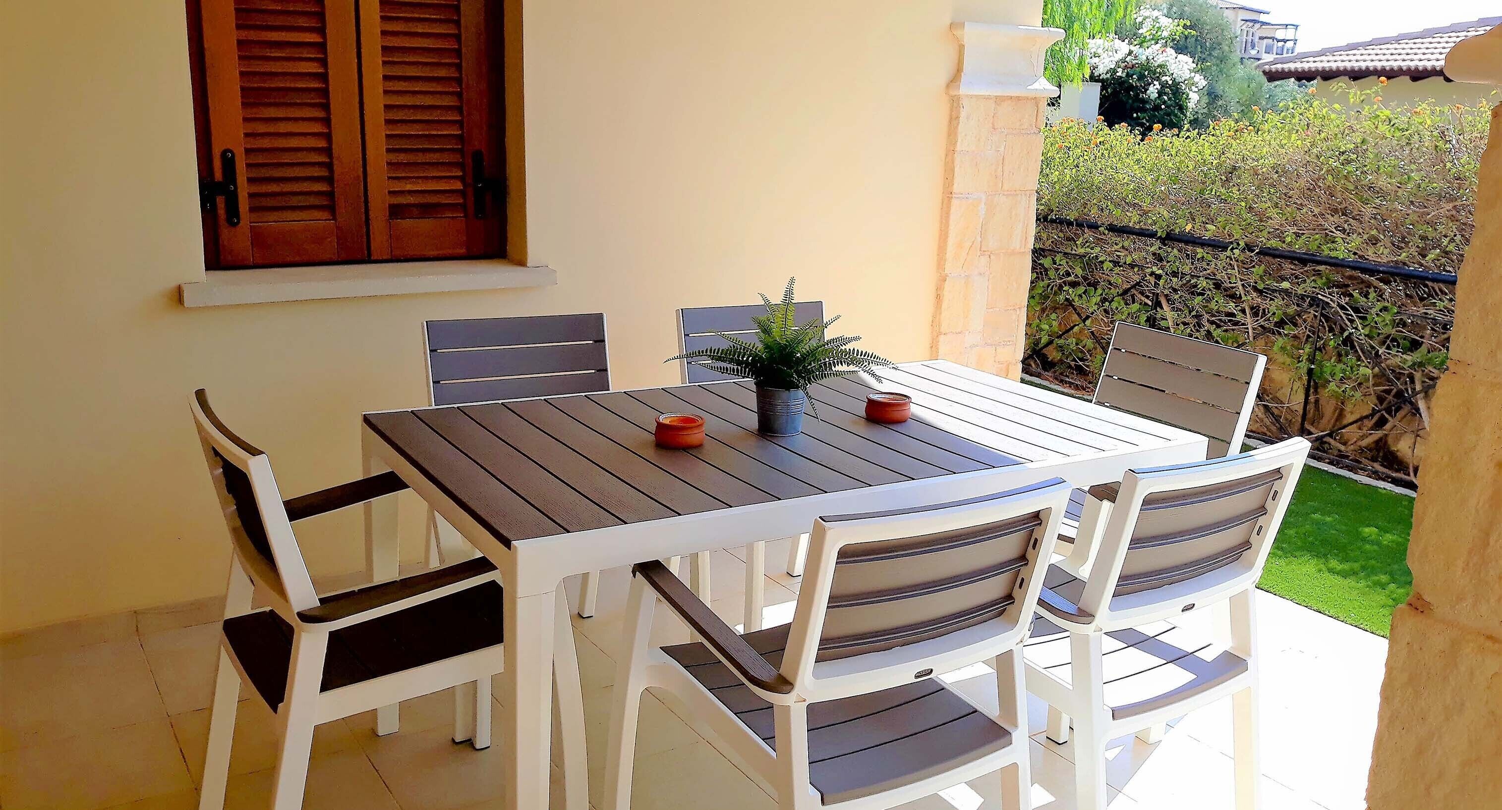 Eine Terrasse mit Tisch und Stühlen, einem Blumentopf und Blick auf einen Garten sowie ein Gebäude im Hintergrund.