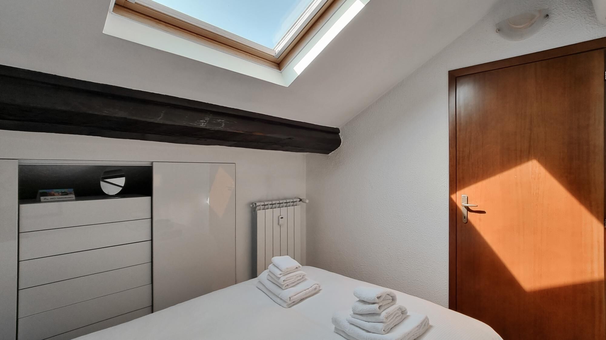 Quarto moderno com claraboia, porta de madeira e guarda-roupa branco.