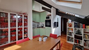 A modern kitchen with green cabinets, a wooden dining table with red chairs, and a bookshelf filled with books. - Italianway Easy - Fauch 9 (Milan)