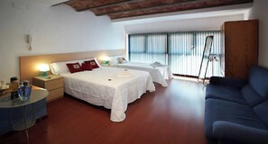 A hotel room with two beds, a blue sofa, a small table with a lamp, and a large window with blinds. - Apartment in Granollers (Granollers)