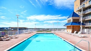Una piscina con sillones de descanso, una torre de salvavidas y un edificio con balcones.