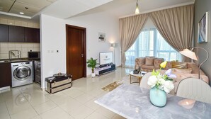 Una sala de estar moderna con un sofá, una mesa de centro y un televisor. Hay una zona de cocina con lavadora y armarios.