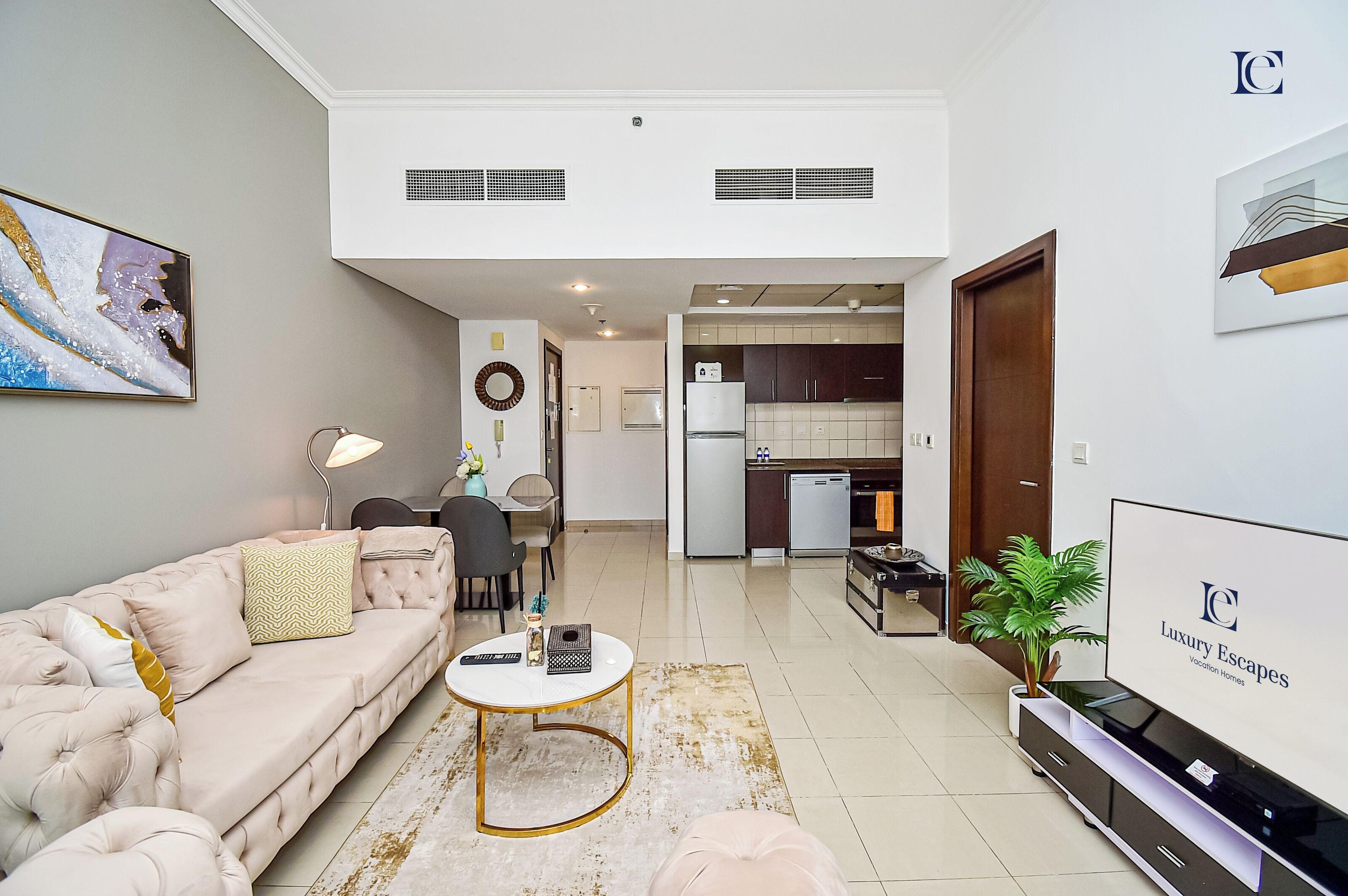 A modern living room with a sofa, coffee table, and TV. There is a kitchen in the background with cabinets and appliances.