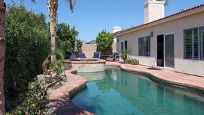 Una piscina de borde curvo, rodeada por una zona de patio con sillones de descanso.