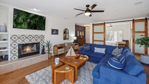 Una sala de estar moderna con chimenea, sofá azul, mesa de centro de madera y una pantalla de televisión grande.