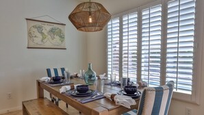 Un comedor con una mesa de madera dispuesta para cuatro, sillas azules a rayas, un mapa del mundo colgante y una lámpara colgante de mimbre.