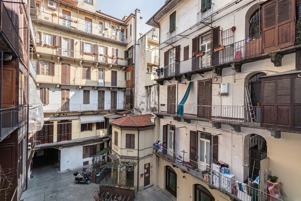 Une rue étroite en milieu urbain, bordée d’immeubles à plusieurs étages, de balcons et où est garée une moto.