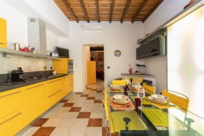 Une cuisine de taille modeste avec des meubles de couleur jaune, un carrelage à motifs et un coin repas comprenant une table en verre et des chaises jaunes.