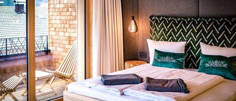 Habitación de hotel con una cama grande, vistas al exterior, suelo de madera y un balcón con sillas.
